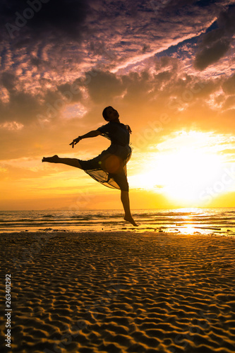 Girl jumping and dancing on the beach at sunset silhouettes 