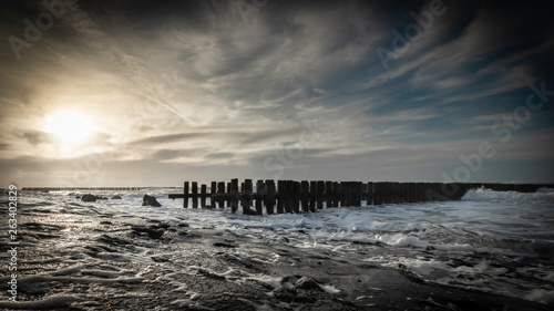 groynes and wave breakers in a turbulent sea just before sunset at a Dutch coast