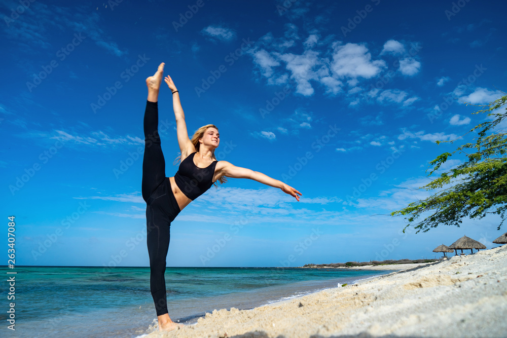 Obraz premium Blond young girl wearing black tights doing dancing poses on the beach. Summer day and happy holiday concept.