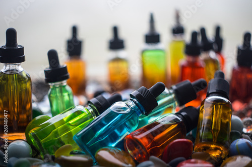 Vape concept. Beautiful colorful vape liquid glass bottles outdoor on stones. Useful as background or electronic cigarette advertisement.