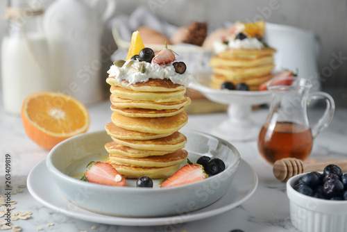Beautiful dessert, fresh pancakes with blueberries, strawberries, orange, honey and whipping cream on plate. Concept of Cooking ingredients and method and plating, Dessert recipes and homemade.