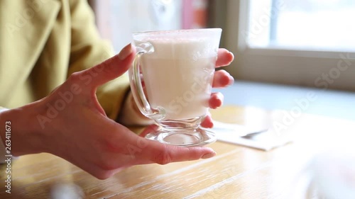 A glass beaker with hot foamed milk. Woman warms hands on a glass mug of hot milk in a cafeshop. Beautiful latte with a big foam. A woman touches a glass with a hot latte photo