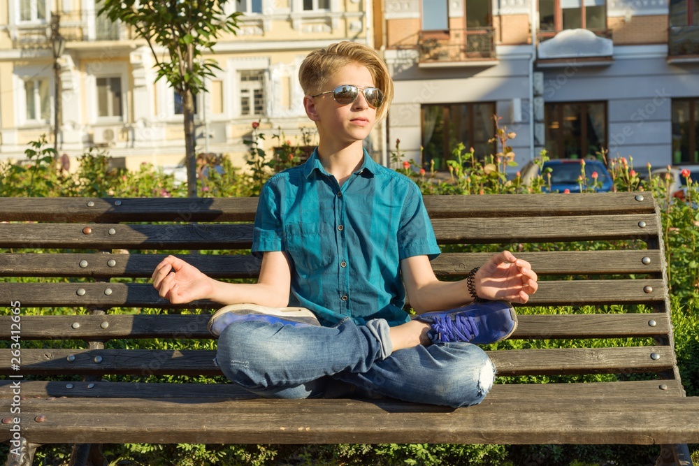 Yoga in city, teenage boy sits in lotus pose on bench in city park. Relax, rest, meditation. Yoga in city, teenage boy sits in lotus pose on bench in city park. Relax, rest, meditation.