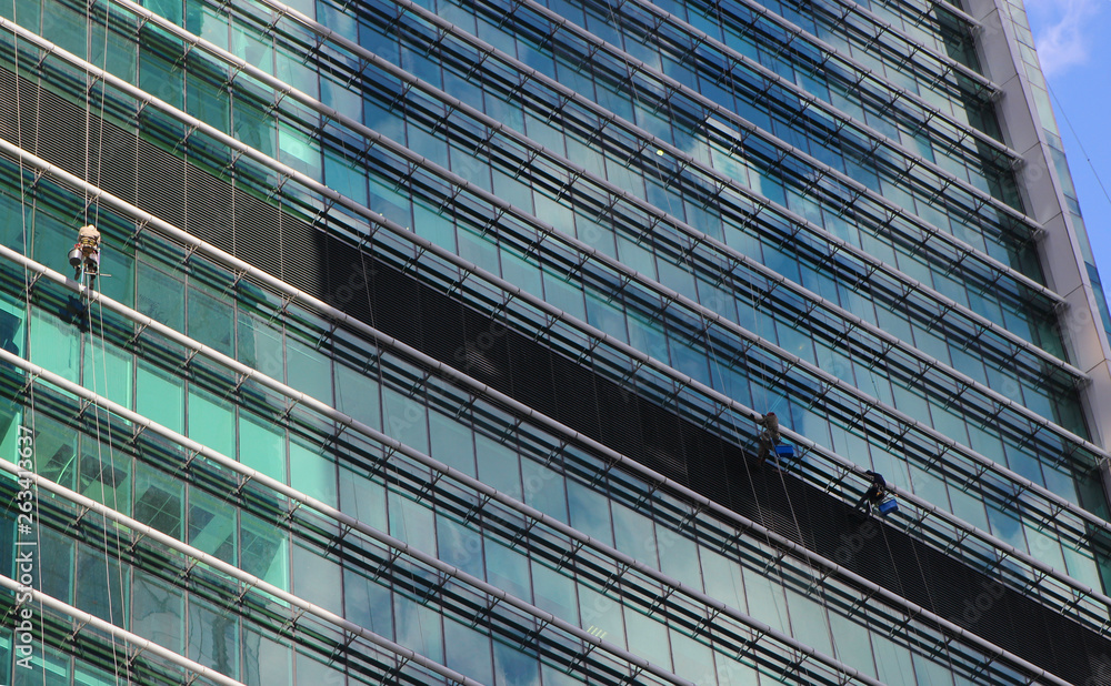 Obraz premium Window washers cleaning the windows of a modern skyscraper in a business district. Cleaning team at work on the facade of an office building
