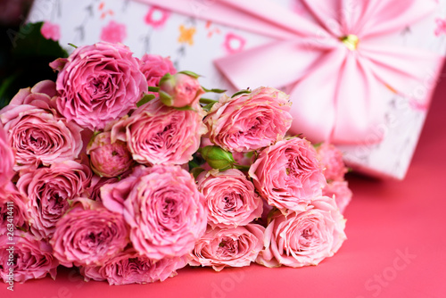 A bouquet of roses and a gift on a pink background