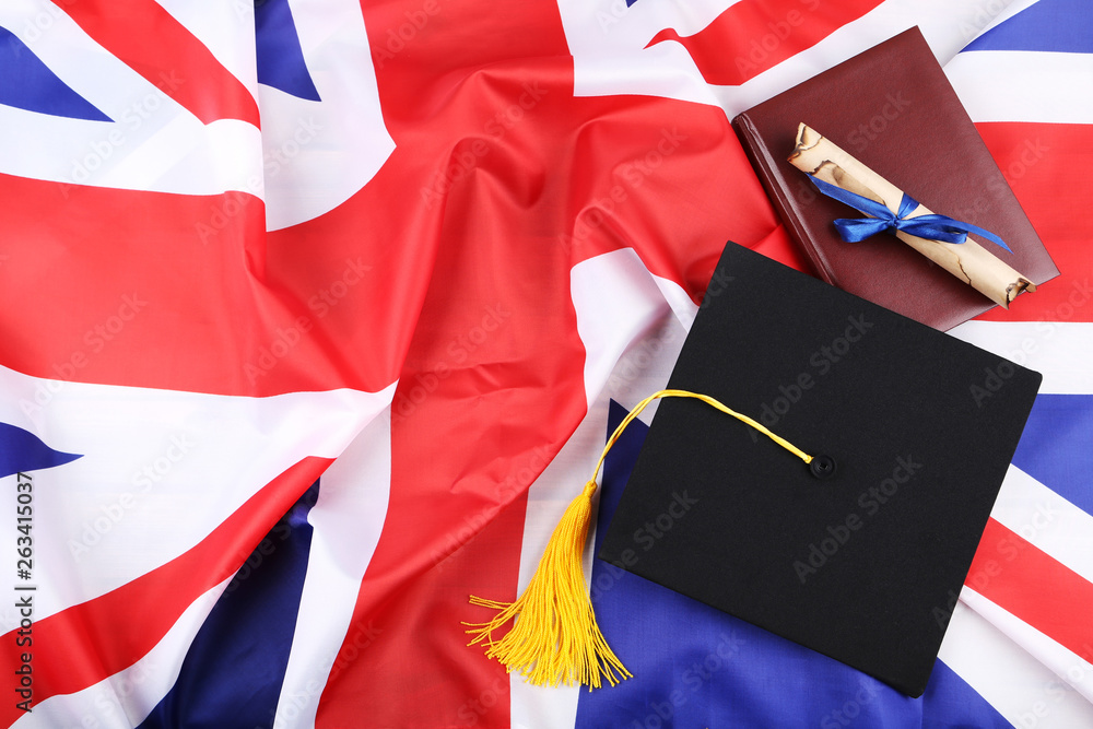 Fototapeta premium Graduation cap with diploma and notepad on British flag background
