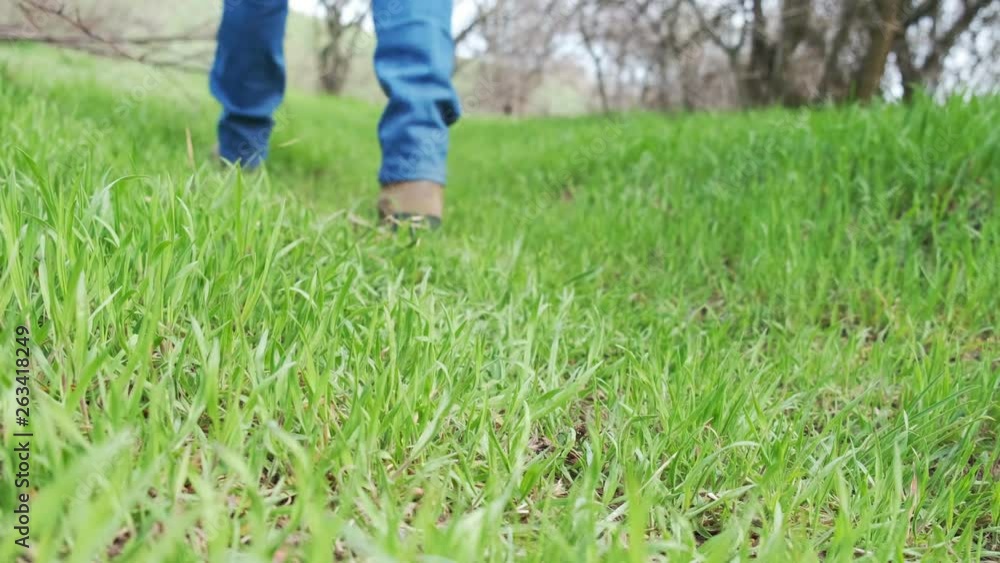 Person wearing boots and walking on the green grass in the forest Person wearing boots and walking on the green grass in the forest