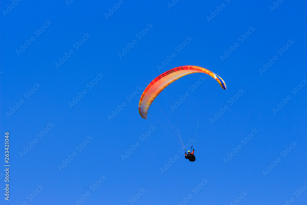 Single colorful paraglider flying in a clear blue sky Single colorful paraglider flying in a clear blue sky