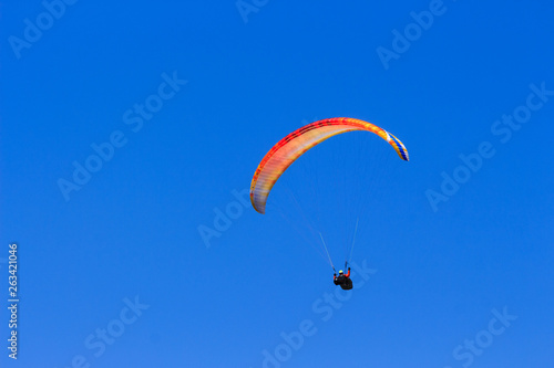 Single colorful paraglider flying in a clear blue sky