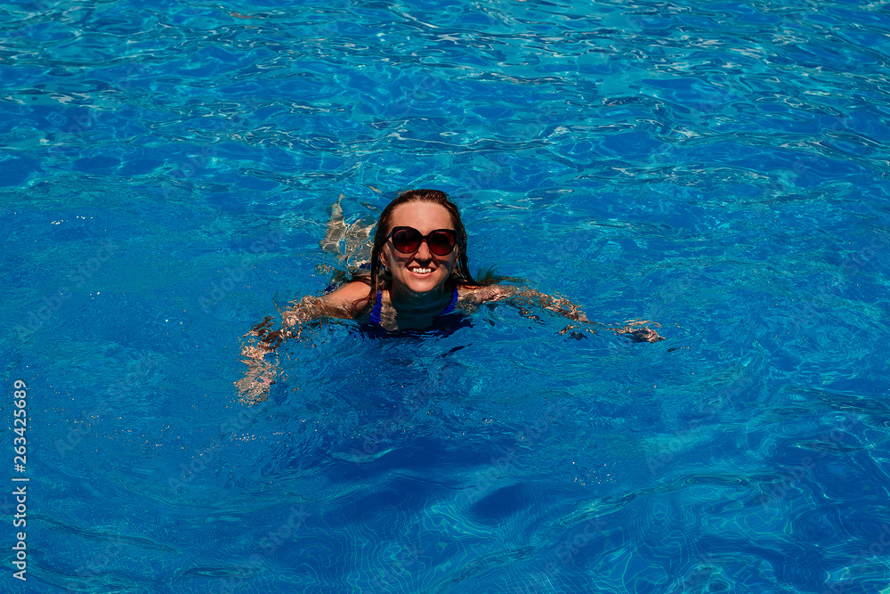 smiling young happy woman swimming in the pool with blue water.