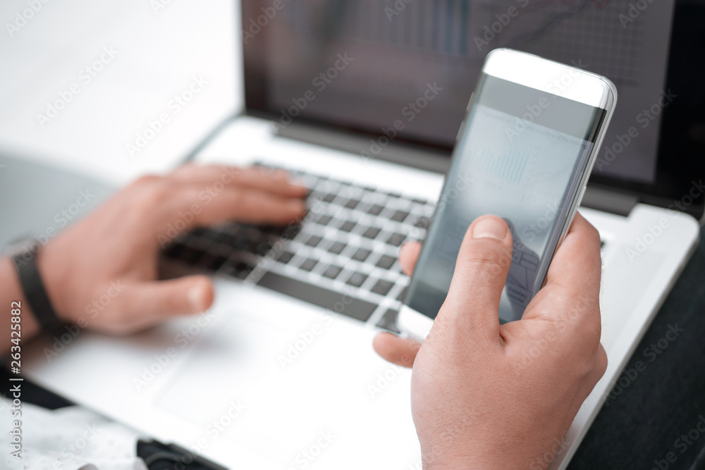 close up. the businessman uses a smartphone and a laptop in the workplace.