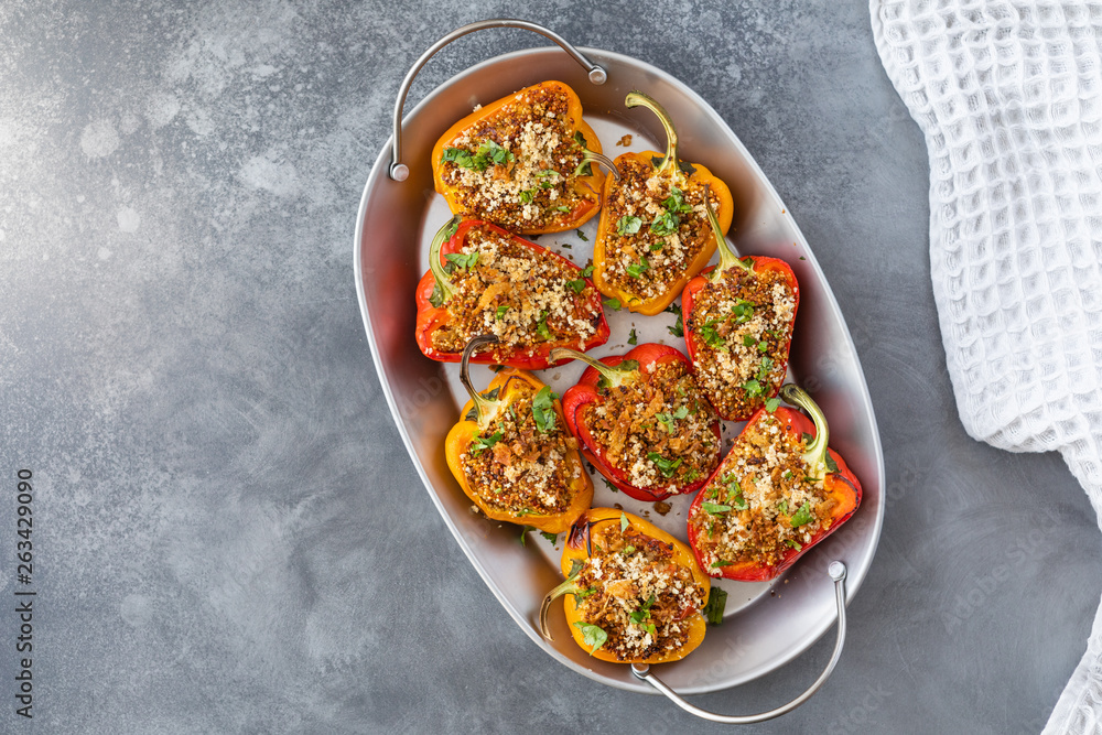 Vegetarian dish with peppers stuffed with quinoa, onion and tomato, sprinkled with walnuts. Top view on gray background - obrazy, fototapety, plakaty 