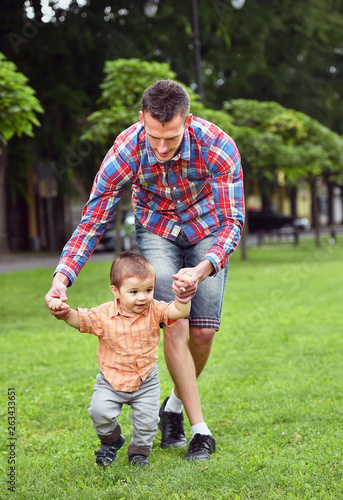 baby boy taking first steps with father help in a park