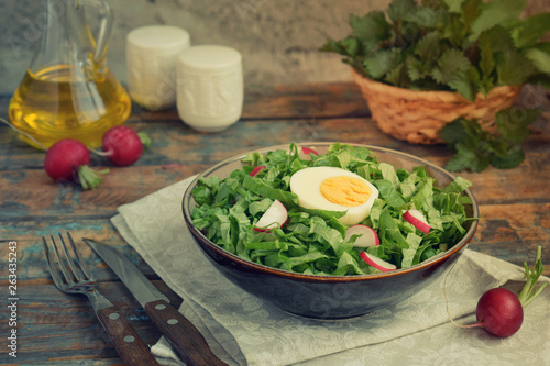 Vitamin salad from lettuce, radish, green onions and eggs, seasoned with vegetable oil in plate on wooden background. Healthy food. Salad of fresh green vegetables