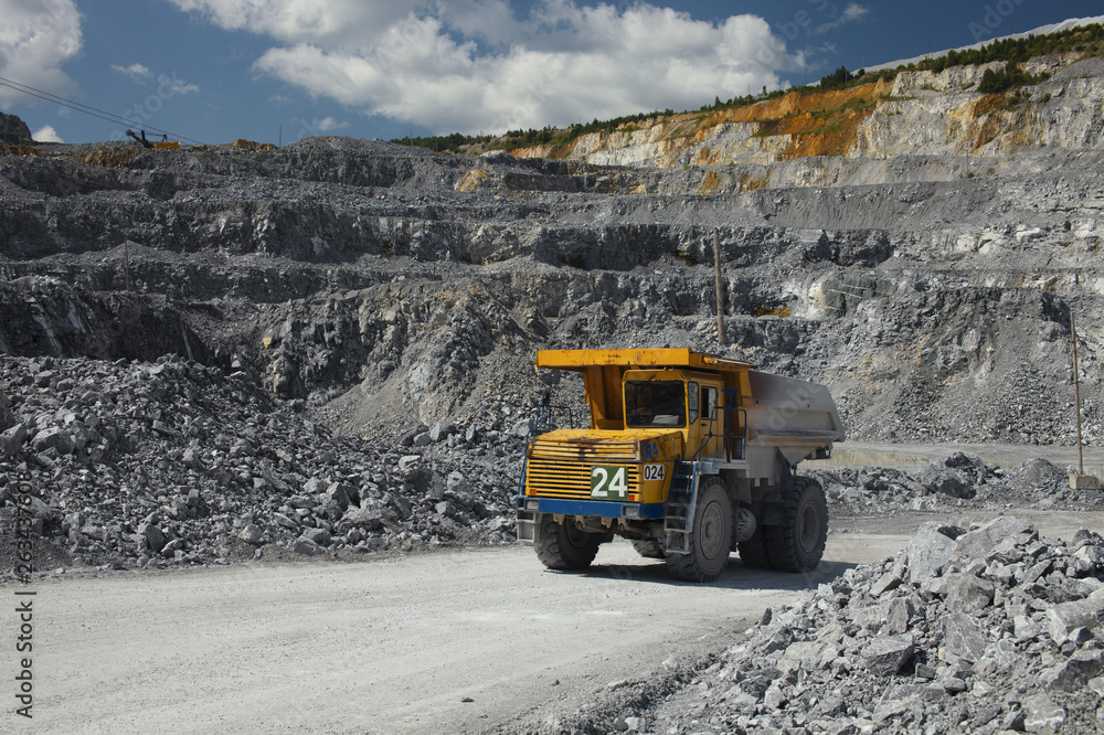 Large multi-toned mining truck in a limestone quarry on the background of blue sky with clouds. Quarry equipment. Mining industry. Large multi-toned mining truck in a limestone quarry on the background of blue sky with clouds. Quarry equipment. Mining industry.