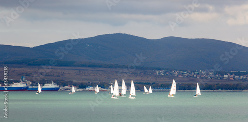 The Resort Of Gelendzhik. Annual children's yacht regatta. Many yachts with white sails in Gelendzhik Bay on the background of the resort and the mountains. Markoth ridge. 
