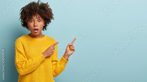 Konstfotografi Photo of astound good looking woman shouts from shocking news, points on right empty corner, wears yellow jumper, surprised by unexpected price, shows something in studio