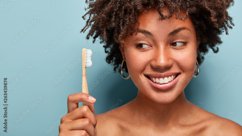 © wayhome.studio - Teeth care and oral hygiene concept. Positive young Afro American woman with curly haircut, holds wooden toothbrush, cleans teeth, has dark skin, being in high spirit. Healthcare and dentistry © wayhome.studio - Teeth care and oral hygiene concept. Positive young Afro American woman with curly haircut, holds wooden toothbrush, cleans teeth, has dark skin, being in high spirit. Healthcare and dentistry