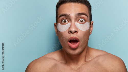 Half naked muscular man with astonished expression, opens mouth widely, has patches under eyes, stunned by late time. Cosmetics and care for men. Shocked man has beauty treatments. Horizontal shot