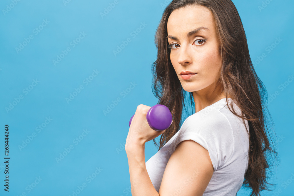 Healthy lifestyle! Side view portrait of a pretty young sportswoman doing exercises with dumbbells isolated on a blue background. Healthy lifestyle! Side view portrait of a pretty young sportswoman doing exercises with dumbbells isolated on a blue background.