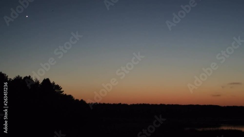 First star in the sunset evening sky over the calm lake in slow motion panoramic 4K video with no people.