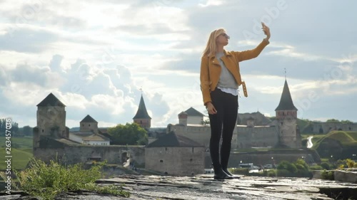 Beautiful blonde young woman taking selfies against gorgeous fortress on sunny summer day. photo