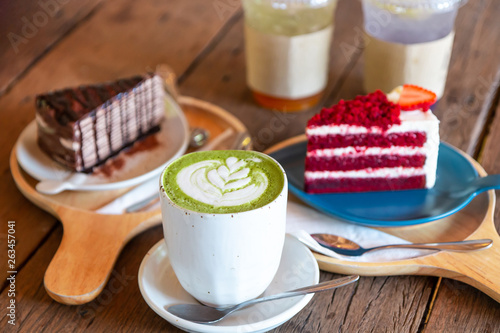 Hot green tea matcha latte with red velvet soft cake and chocolate cake on a wooden table at the coffee shop.