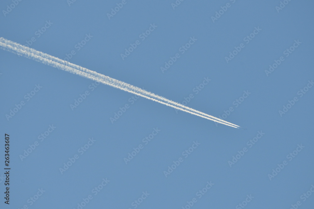 Commercial aircraft at very high altitude with white contrail on cloudless blue sky Commercial aircraft at very high altitude with white contrail on cloudless blue sky