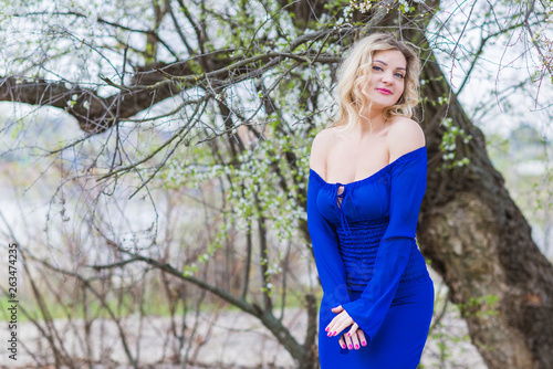 Romantic woman in blue dress at spring blossom garden. Concept of plus size woman and tenderness, modern beauty or femininity   © T.Den_Team