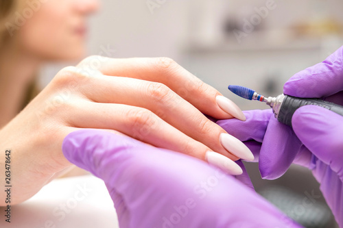 Fototapeta Manicurist work on a woman client hands, make her nails look beautiful
