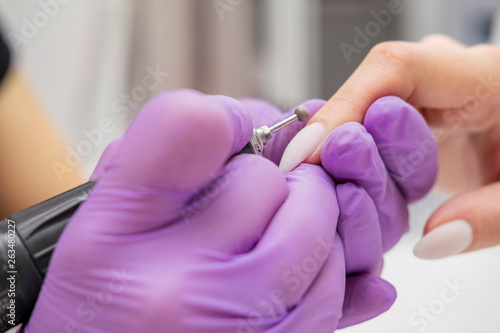 Manicurist work on a woman client hands  make her nails look beautiful. Salon procedure in process. Professional works in gloves using drill for sterility