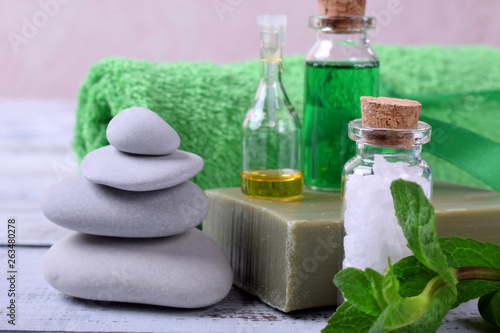 Spa set: massage stones, aromatic oil, sea salt, green gel, organic soap and green towel on white wooden table