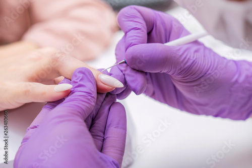 Manicurist work on a woman client hands  make her nails look beautiful. Salon procedure in process. Professional works in gloves for sterility