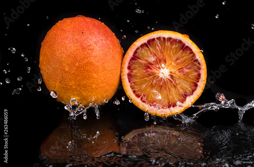 Fototapeta Naklejka Na Ścianę i Meble -  Bloody orange whole and halves, slices with reflection on white and black background in a spray of water