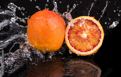 Fototapeta Naklejka Na Ścianę i Meble -  Bloody orange whole and halves, slices with reflection on white and black background in a spray of water