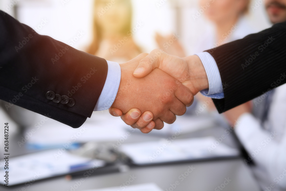 Business people shaking hands at meeting while theirs colleagues clapping and applauding. Group of unknown businessmen and women in modern white office. Success teamwork, partnership and handshake Business people shaking hands at meeting while theirs colleagues clapping and applauding. Group of unknown businessmen and women in modern white office. Success teamwork, partnership and handshake