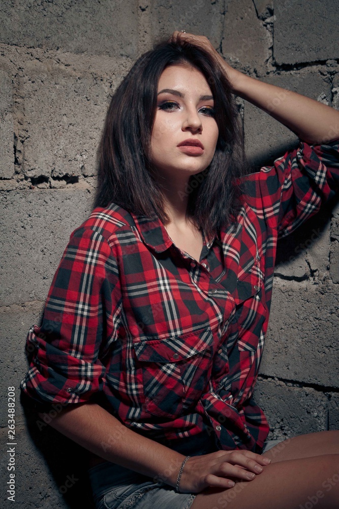 Girl in an abandoned building sits on concrete in jeans with a tattoo Girl in an abandoned building sits on concrete in jeans with a tattoo