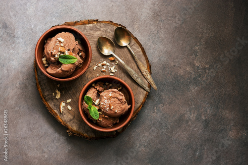 Homemade chocolate ice cream with mint and nuts in bowls on a stump cutting board, dark rustic background. Overhead view, copy space.