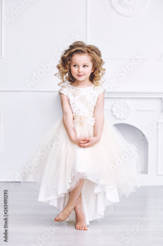 Little beautiful and cute girl child in a fashionable festive dress in a white interior