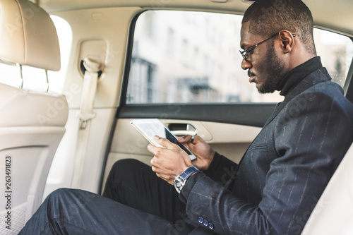 Young businessman using tablet while sitting in the backseat of a car. © xartproduction