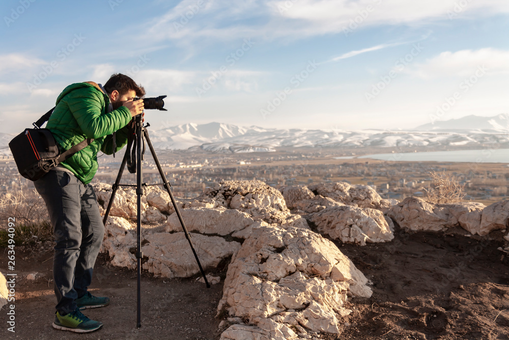 Travel photographer man taking nature video of mountain landscape. Professional videographer on adventure vacation shooting slr camera on tripod.