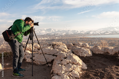 Travel photographer man taking nature video of mountain landscape. Professional videographer on adventure vacation shooting slr camera on tripod.