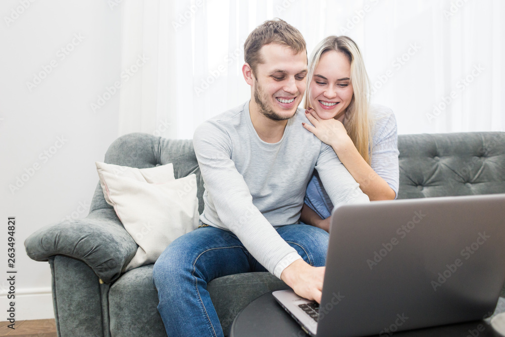 Young beautiful couple resting on the couch and watching online video from a laptop in the living room.
