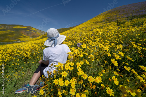Beautiful woman with back facing camera  sitting in a field of yellow wildflowers. Concept for spring allergy season