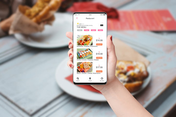 Woman in the restaurant ordering food with app on her phone, blurred table with food in background