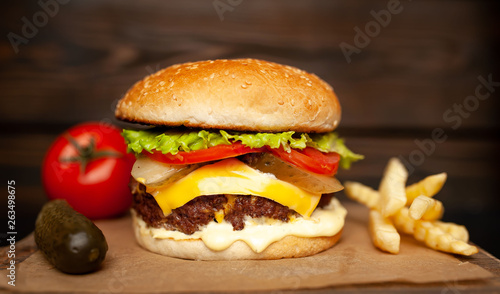  Delicious homemade hamburger made of beef, salad, cheese, cucumber and french fries on a wood background