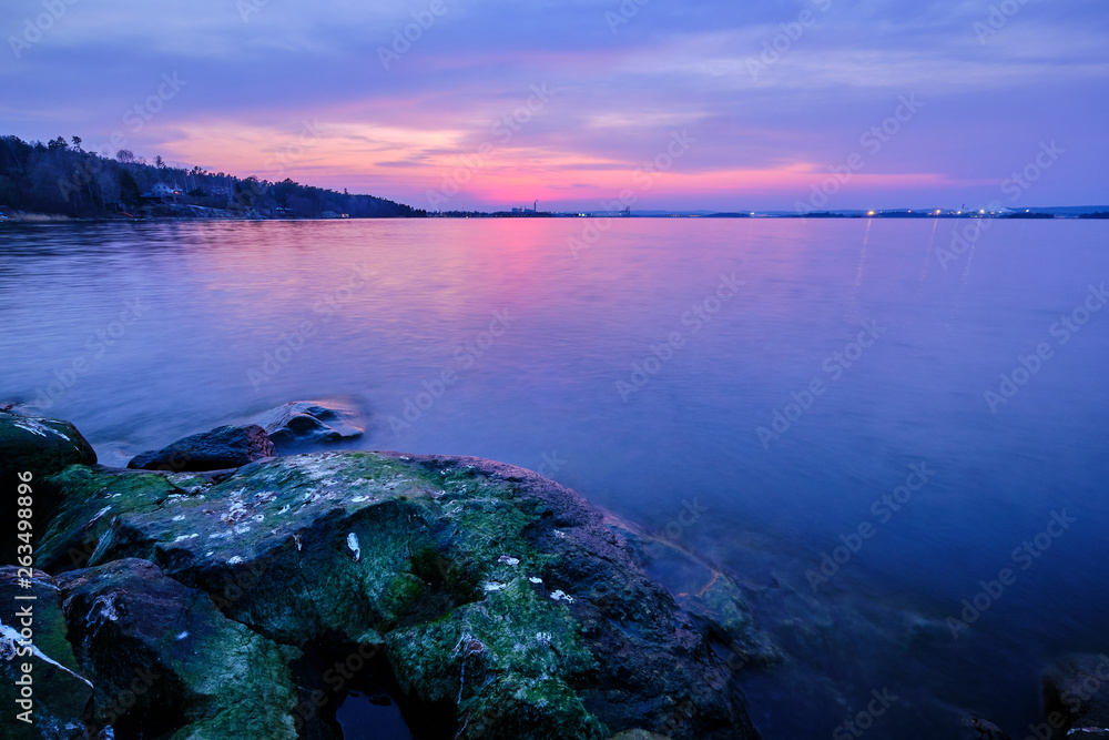 stone with moss in the foreground and sea after sunset in the background