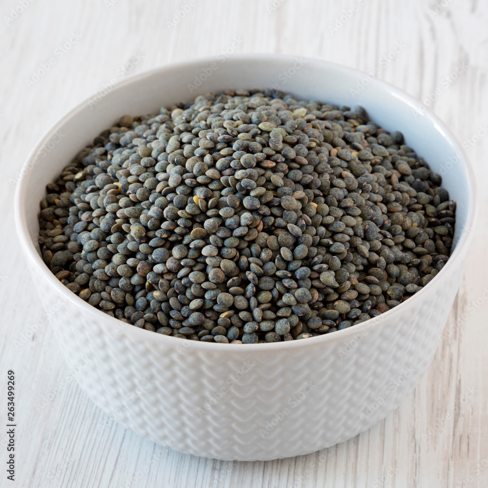 Dry green french lentils in a bowl over white wooden surface, side view. Close-up. Dry green french lentils in a bowl over white wooden surface, side view. Close-up.