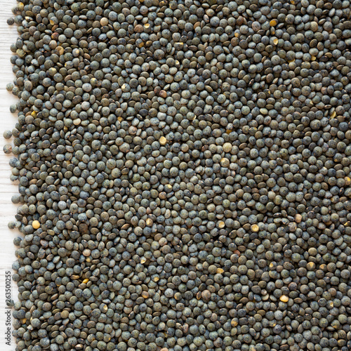 Dry green french lentils on a white wooden surface, overhead view. Top view, from above.