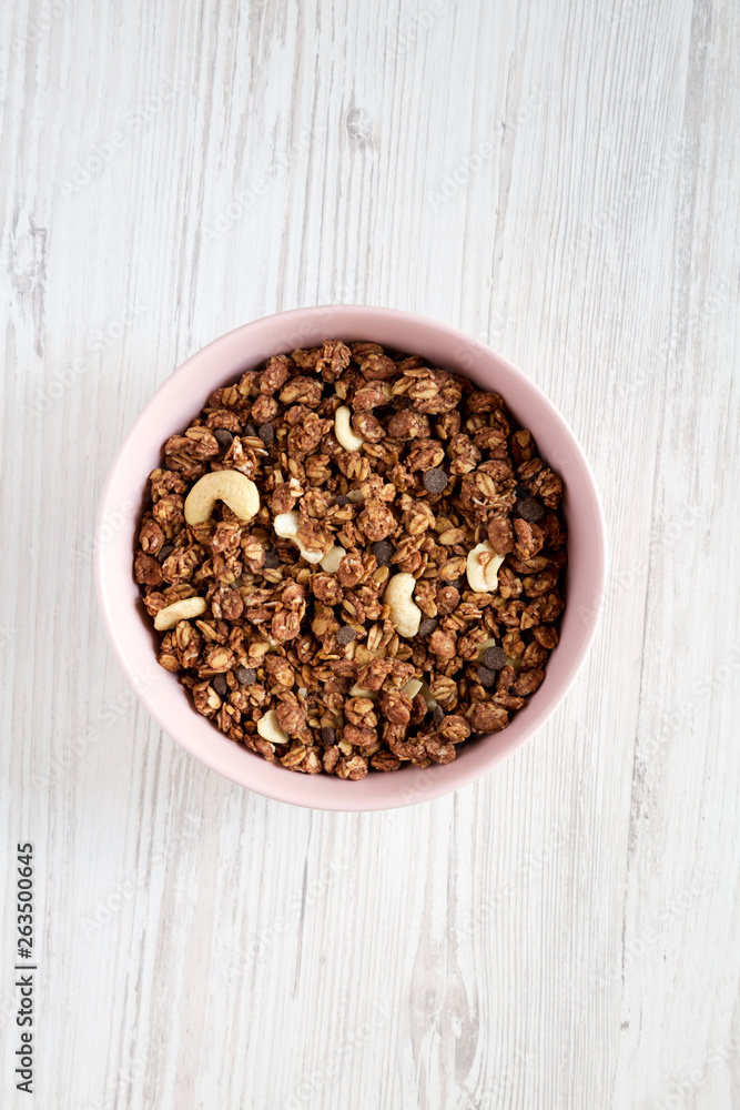 Homemade chocolate granola with nuts in a pink bowl over white wooden background, top view. From above, overhead, flat lay. Homemade chocolate granola with nuts in a pink bowl over white wooden background, top view. From above, overhead, flat lay.